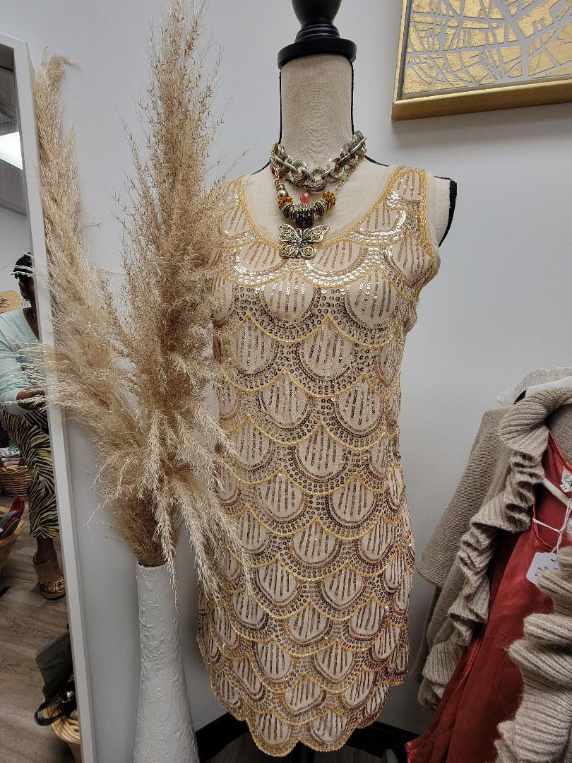 A vintage sequined dress on a dress form in a boutique, with dried pampas grass and framed art behind it